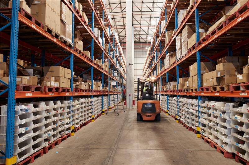 A full warehouse stacked with inventory, with a forklift driving through the isle of pallets.