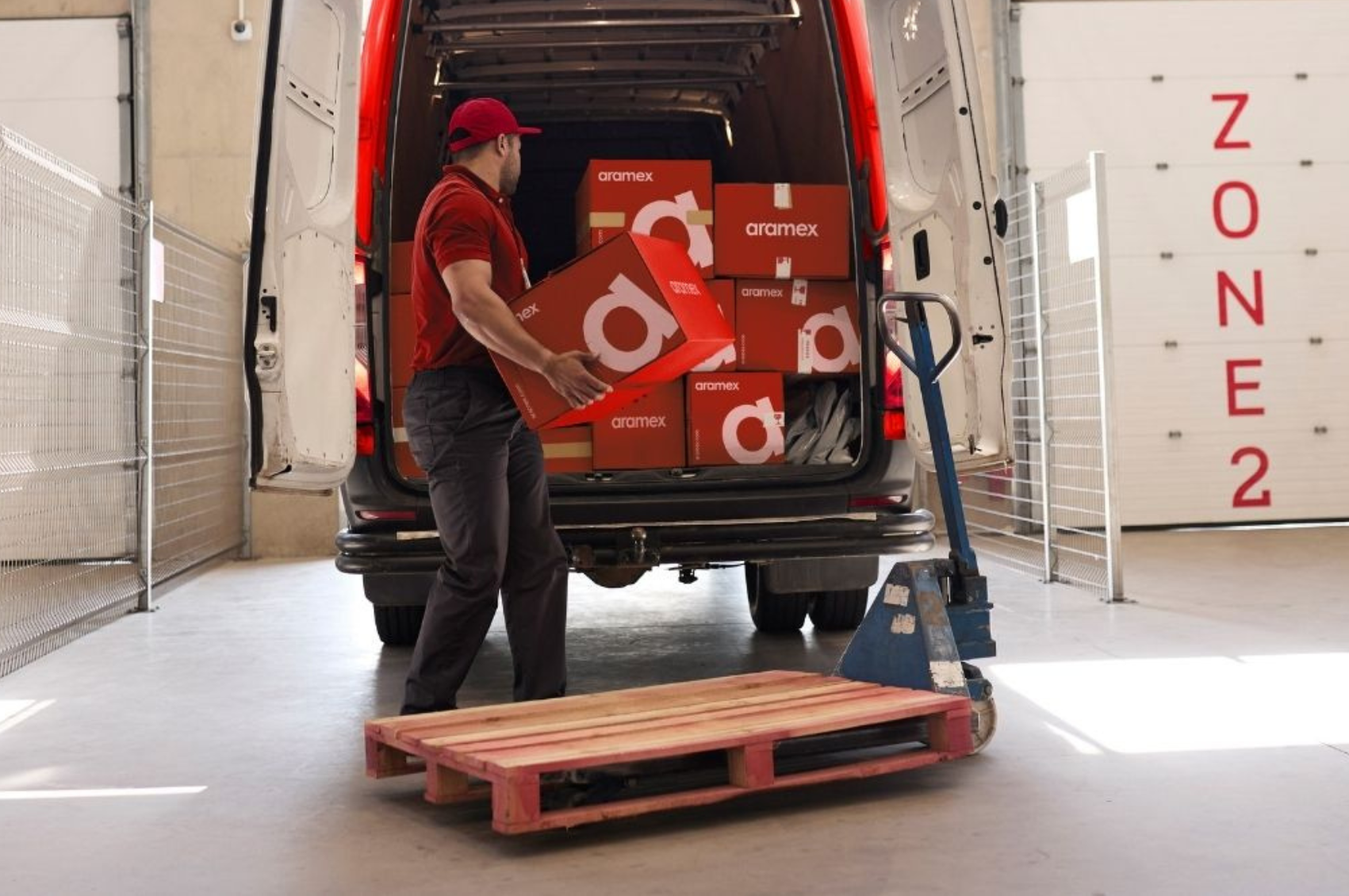 Aramex courier unloading branded packages from a delivery van at a warehouse facility.